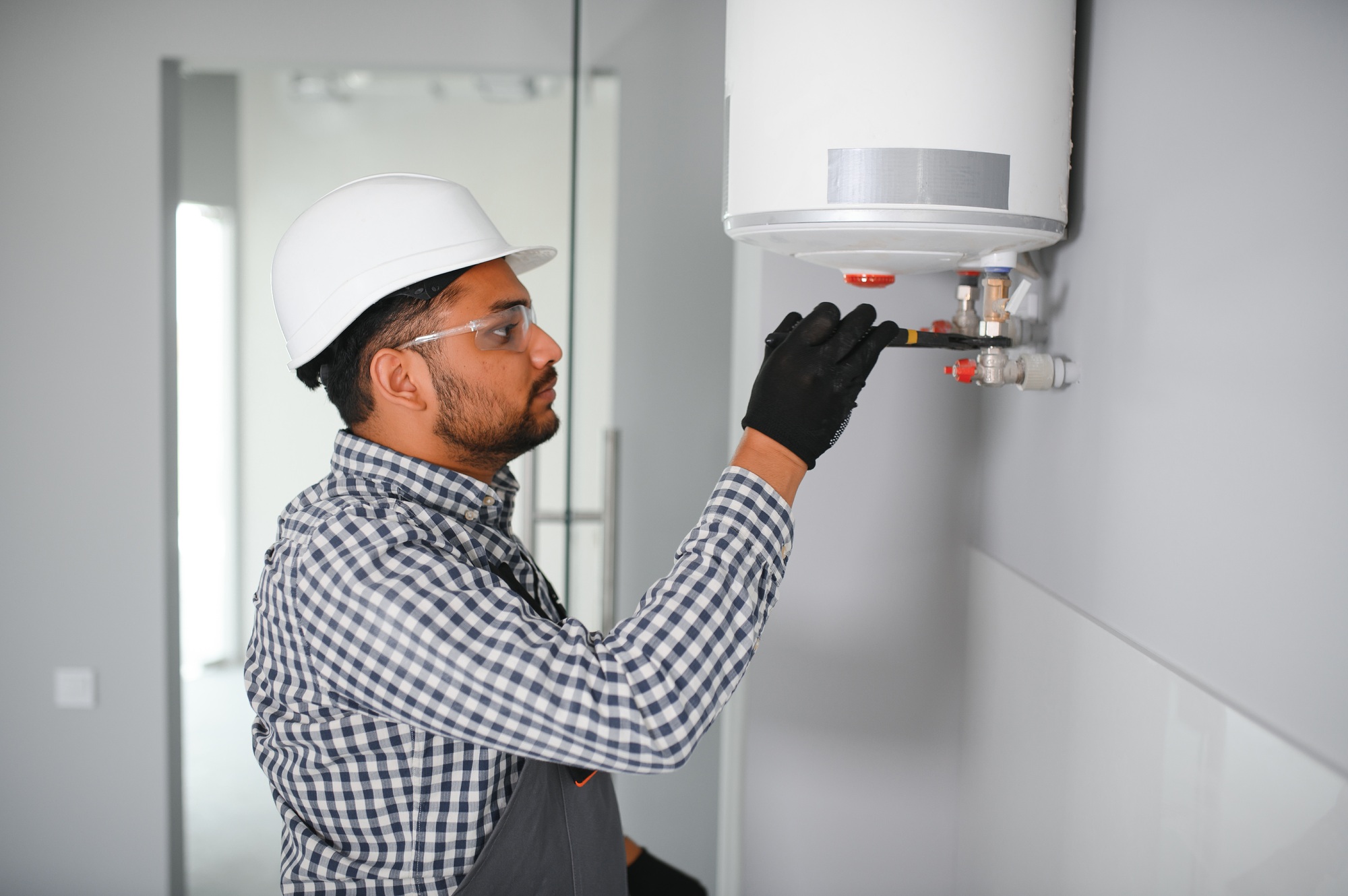 Indian plumber using screwdriver while fixing boiler or water heater, working on heating system
